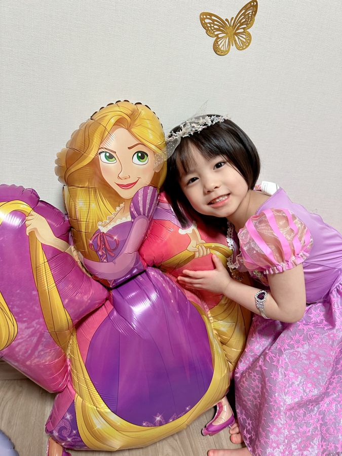 ラプンツェルのドレスを着て、ラプンツェルのキャラクターバルーンに寄り添う5歳女の子