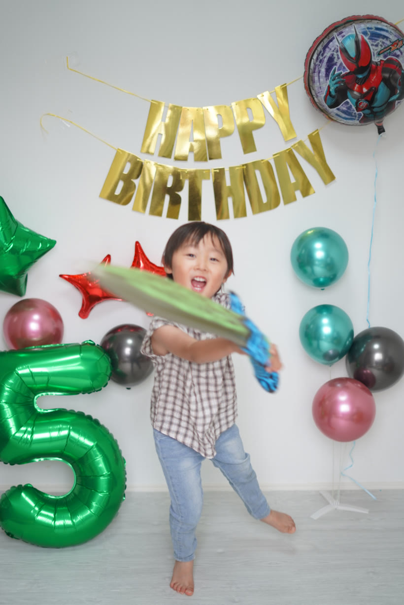 剣のバルーンをカメラに向かって振りながら大笑いする5歳の男の子
