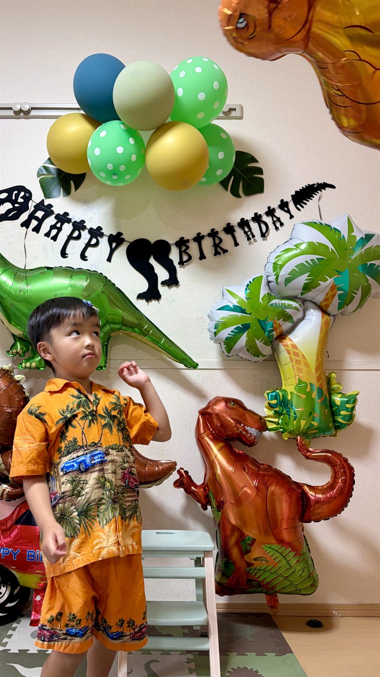 オレンジのアロハシャツを着た男の子が、赤茶色のティラノサウルスのバルーンを見上げている飾り付け実例