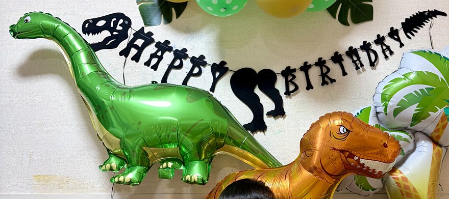 緑のアパトサウルスのバルーンと、恐竜の骨格デザインの黒いHAPPY BIRTHDAYガーランドの寄り写真