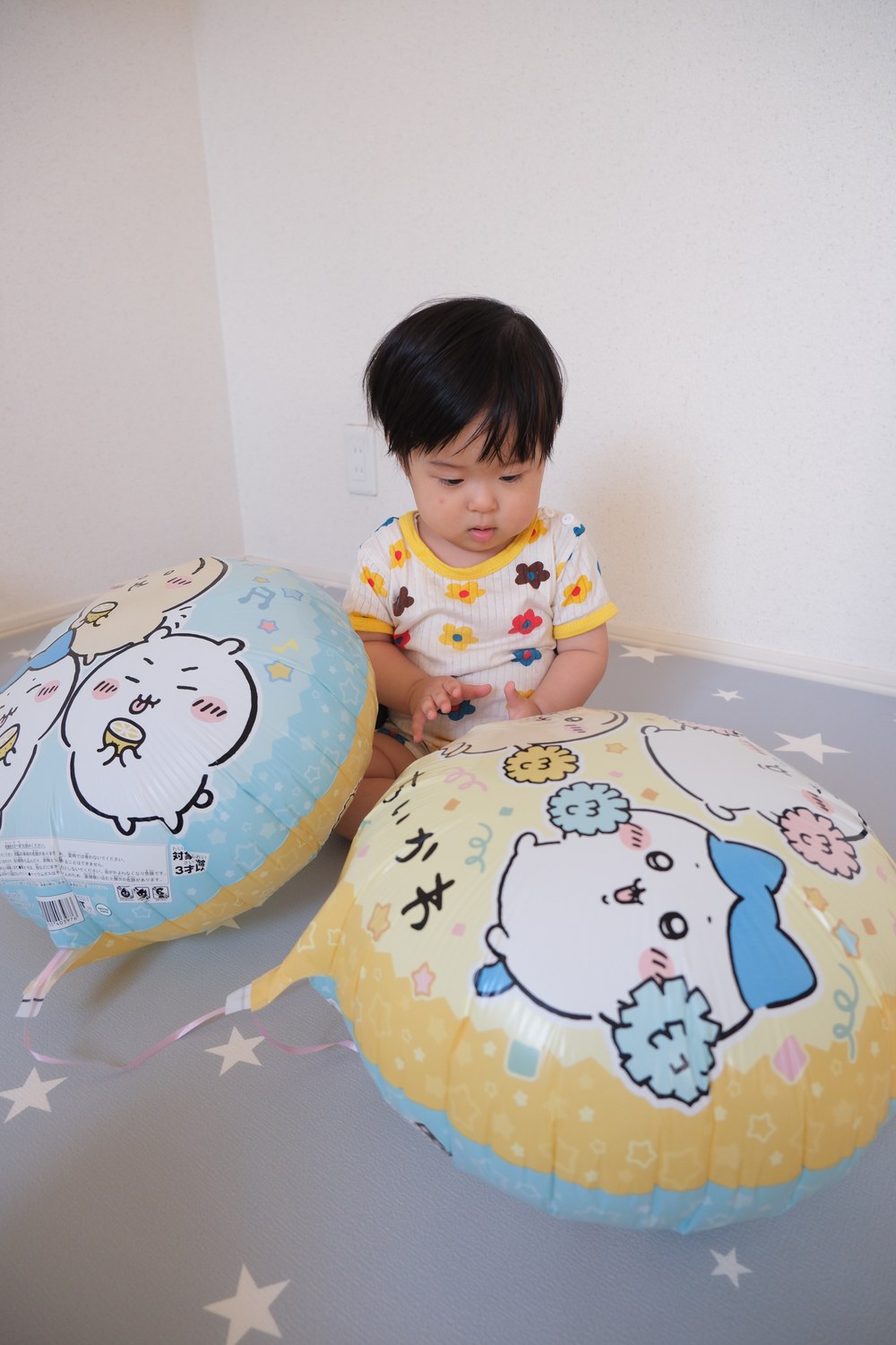 床に置いた2つのちいかわのバルーンのあいだに、お子さまが座っている。左のバルーンは水色の面、右のバルーンはちいかわと書かれた黄色い面が見えている