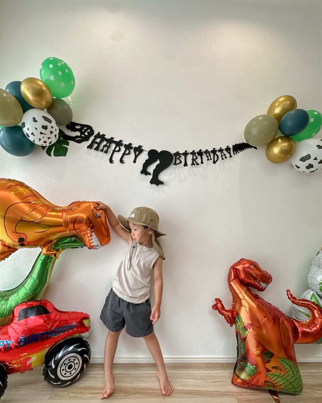 黒い恐竜の骨格ガーランドの下で、子どもが大きな恐竜バルーンの頭に手をのせている誕生日の飾り付け実例