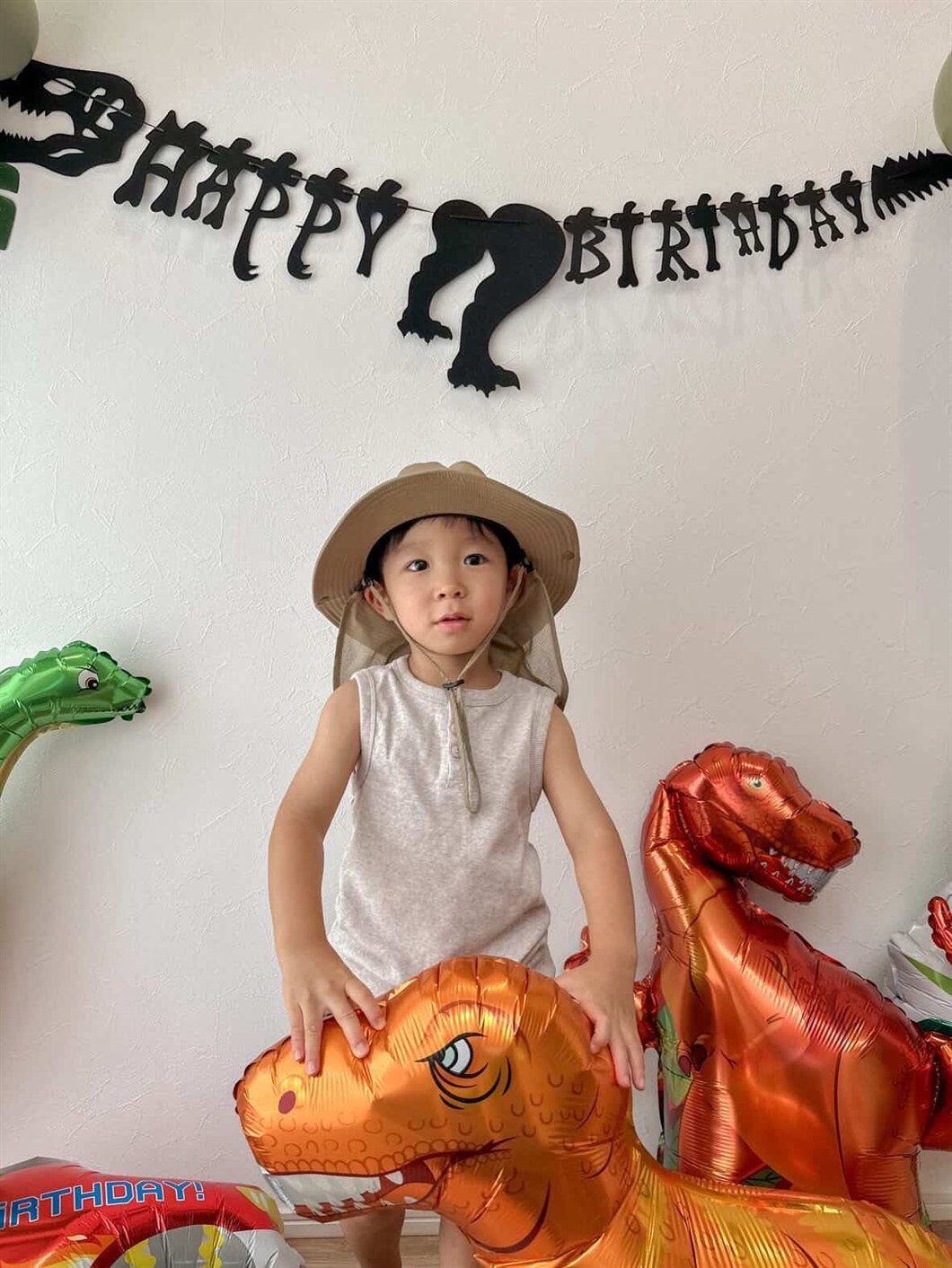 探検帽をかぶった子どもが、床に置かれた恐竜のバルーンを両手で抱えている飾り付け実例