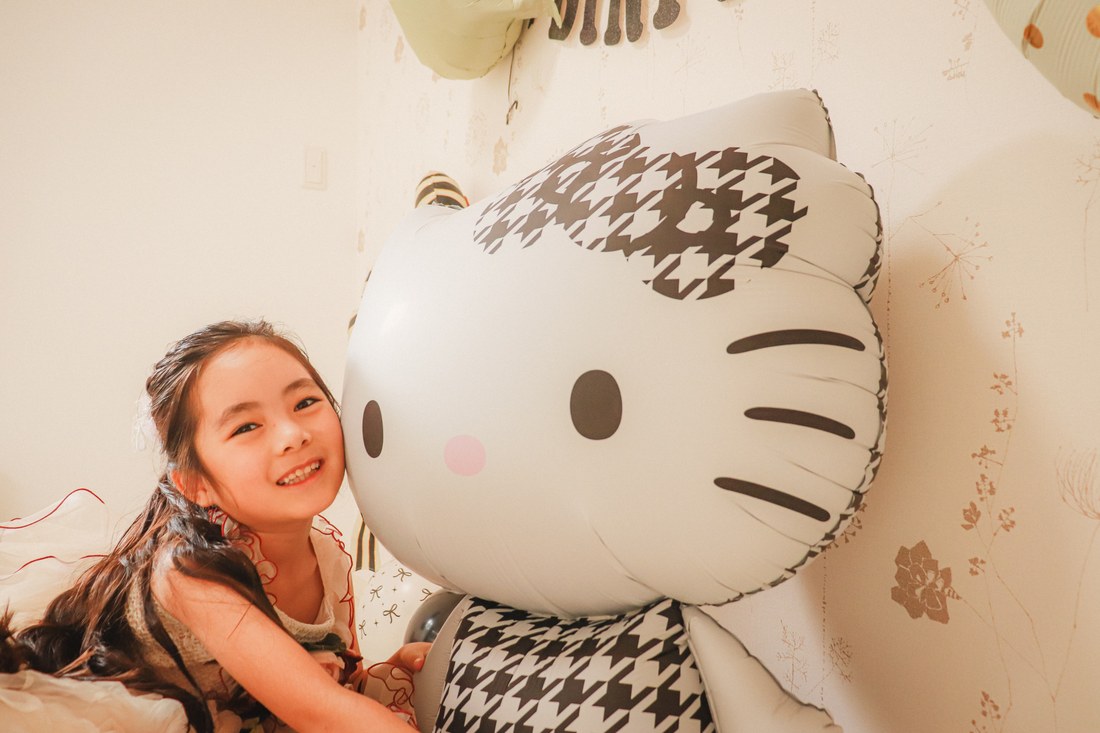 お子さまが千鳥格子のハローキティのバルーンに顔を寄せて、ほっぺをくっつけるようにして笑っている