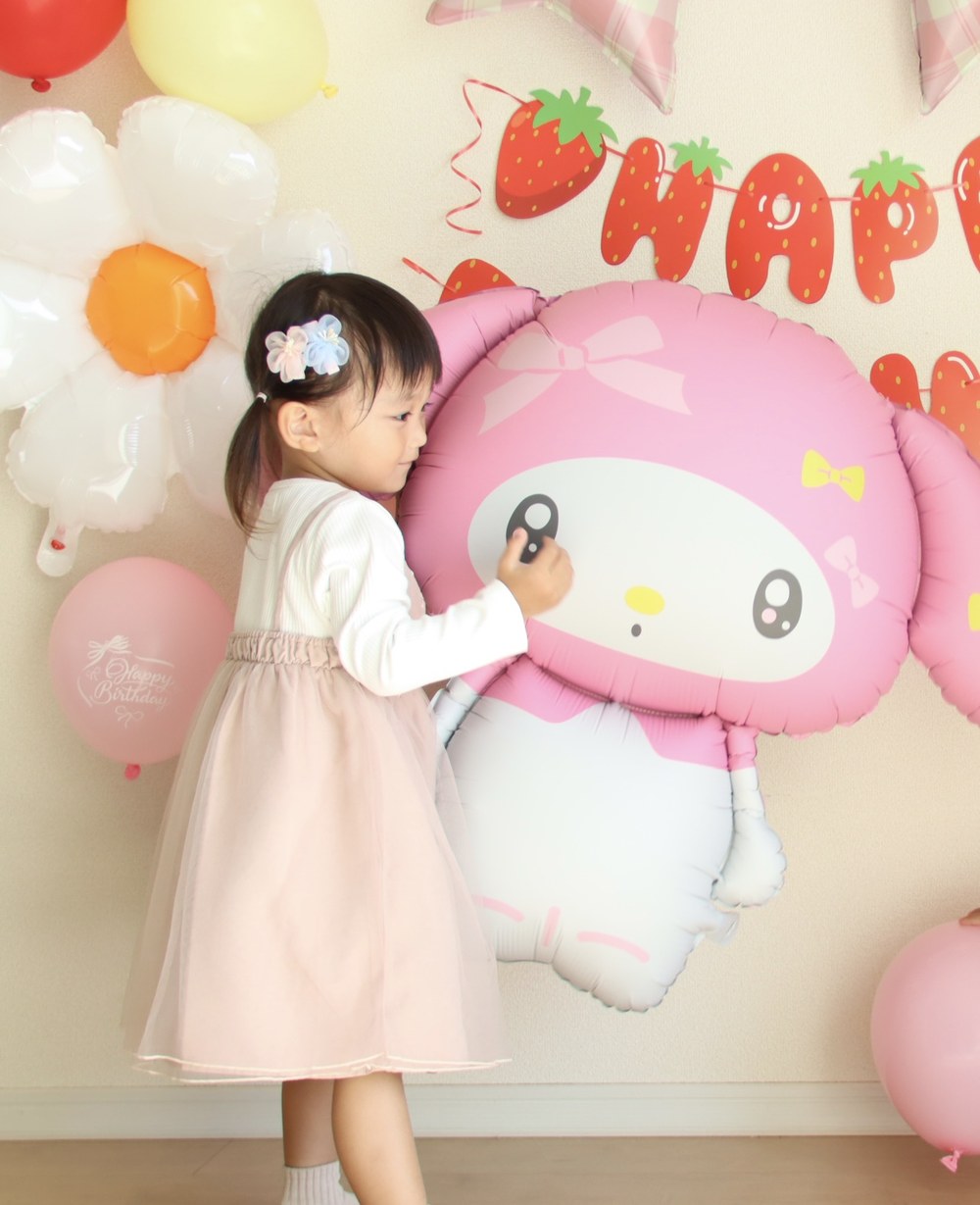床に置いたマイメロディのバルーンの顔に、お子さまが手を伸ばしてそっと触れている横向きの写真