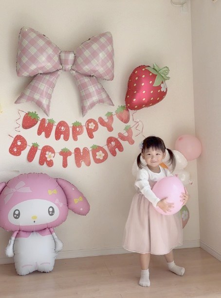 縦長で撮った、いちごマイメロの飾り付け。上にチェックのリボンといちご、中段にHAPPY BIRTHDAYのガーランド、下に床に置いたマイメロディと、ピンクの風船を抱えたお子さま