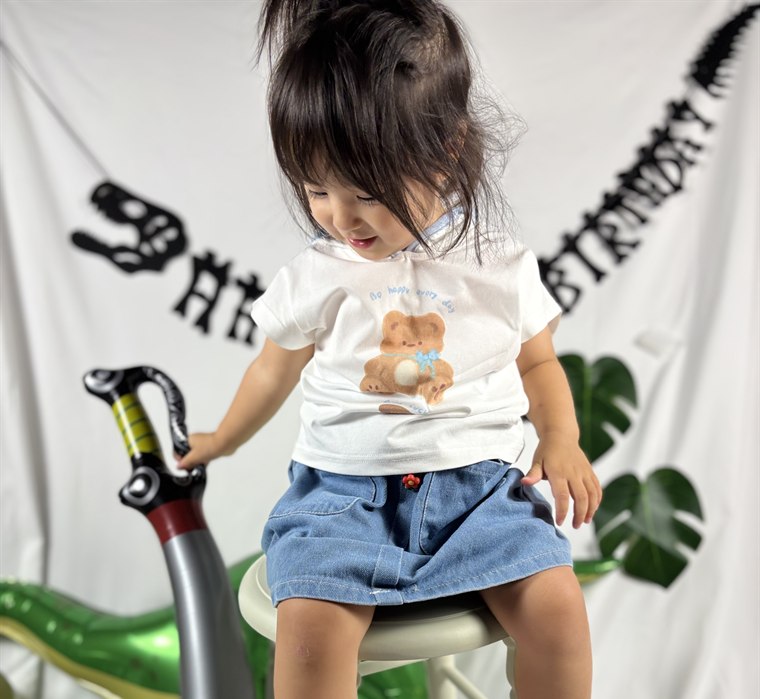 白い布の撮影スペースで丸椅子に座り、恐竜セット付属の剣のバルーンを持つ女の子
