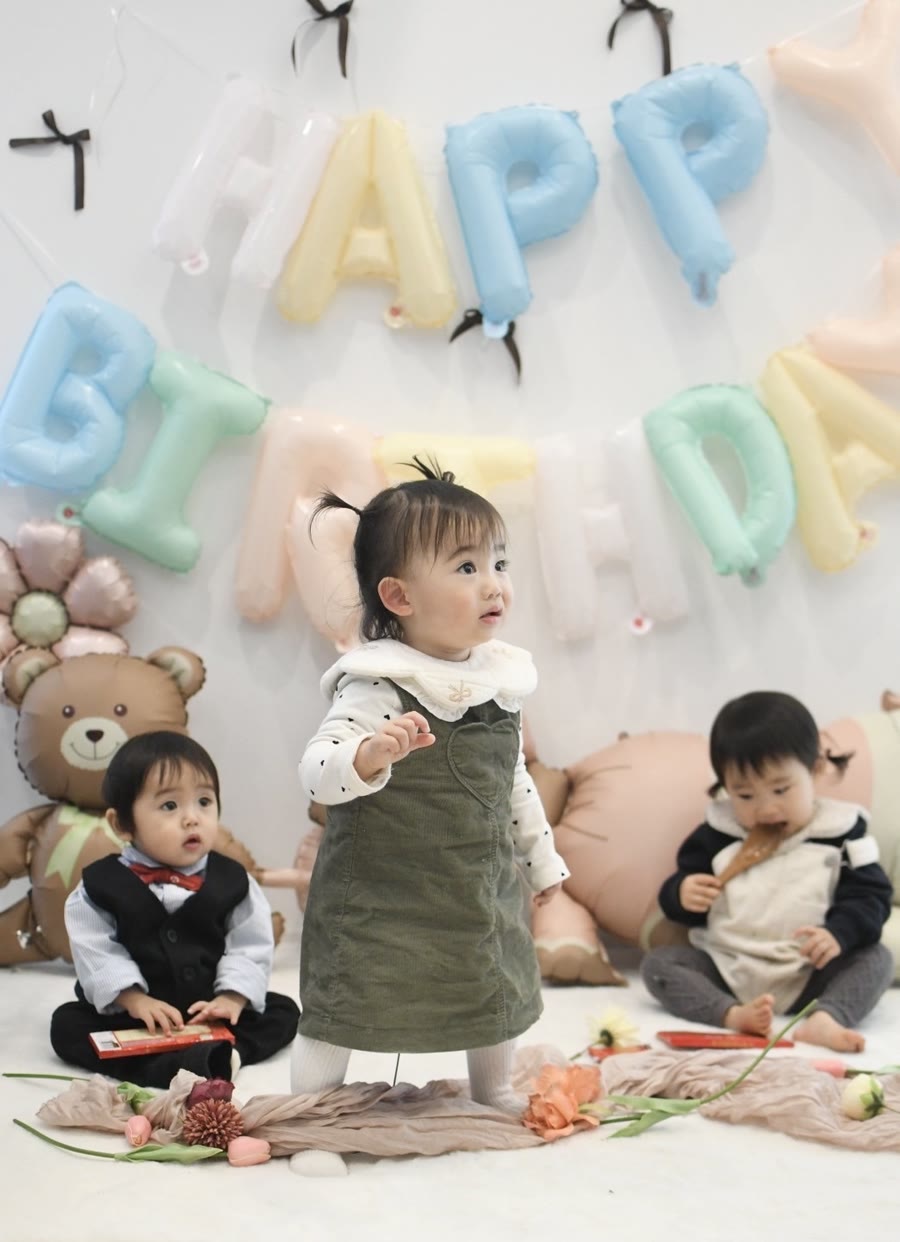 パステルカラーのHAPPY BIRTHDAY文字バルーンとクマや花の動物バルーンの前に集まった1歳の子どもたち