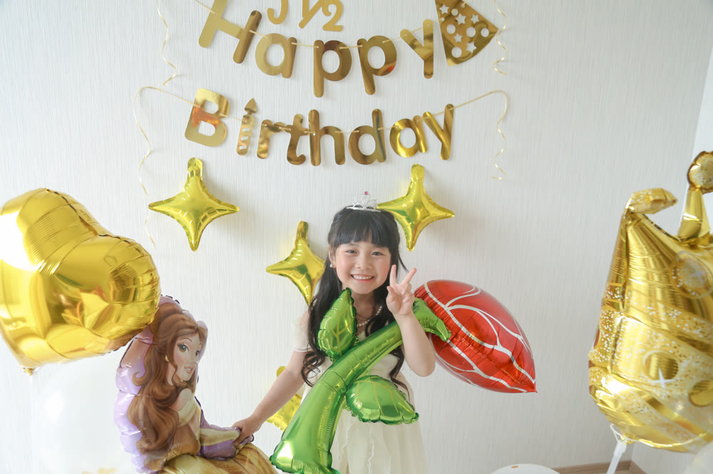 ティアラをつけた女の子がバラのバルーンを抱えて笑っている、ゴールドで統一されたベルの誕生日飾り付け実例