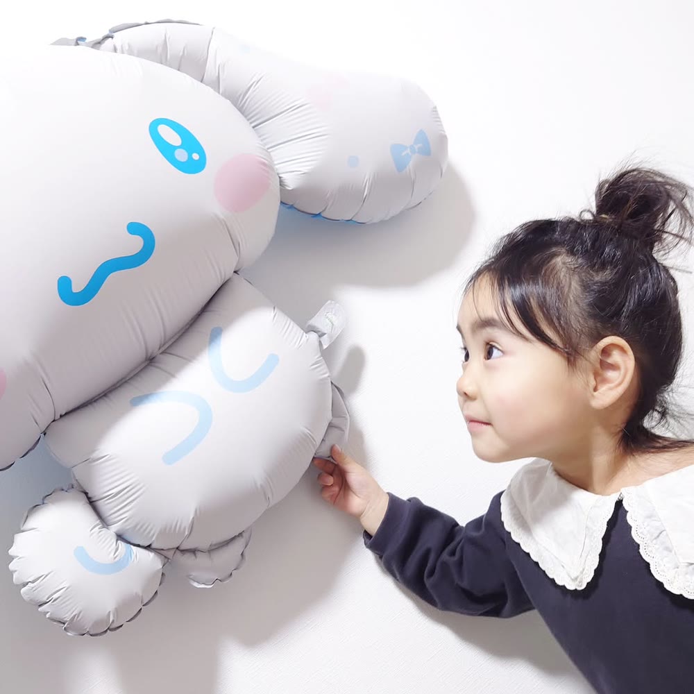 壁に飾った特大シナモロールバルーンに顔を近づけて見つめる小さな女の子
