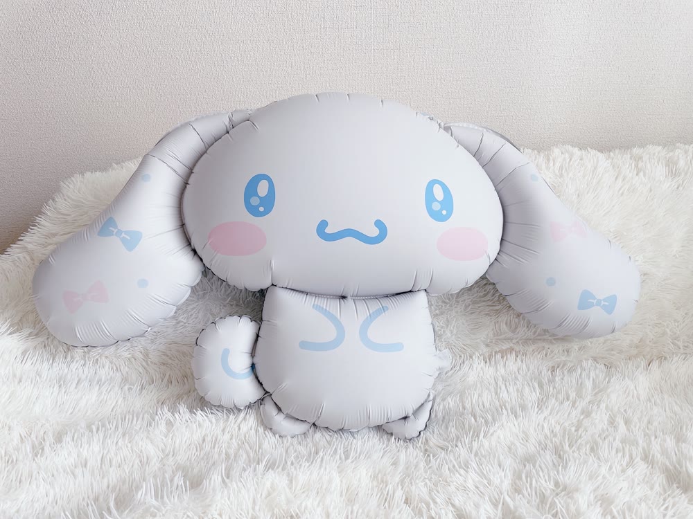ふわふわの白いラグの上に置いた特大シナモロールバルーン。大きな垂れ耳とつや消し加工の質感