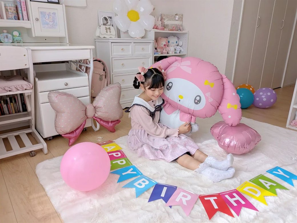 マイメロディ バルーンセットの誕生日飾り付け実例。特大マイメロバルーンを抱える女の子と虹色のガーランド