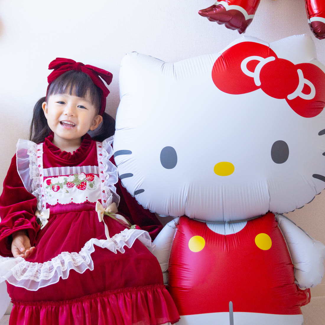 特大ハローキティバルーンの隣に立って笑う赤いドレスの女の子。キティの方が背が高い