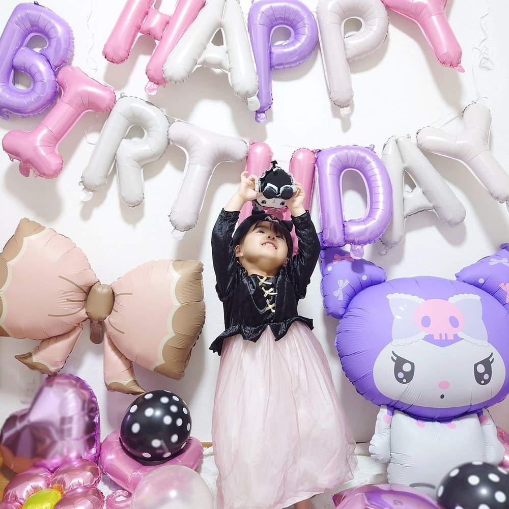 HAPPY BIRTHDAYのバルーンの前で、クロミのぬいぐるみを両手で持ち上げる子ども。右に特大クロミバルーン、足元に黒い水玉のゴム風船