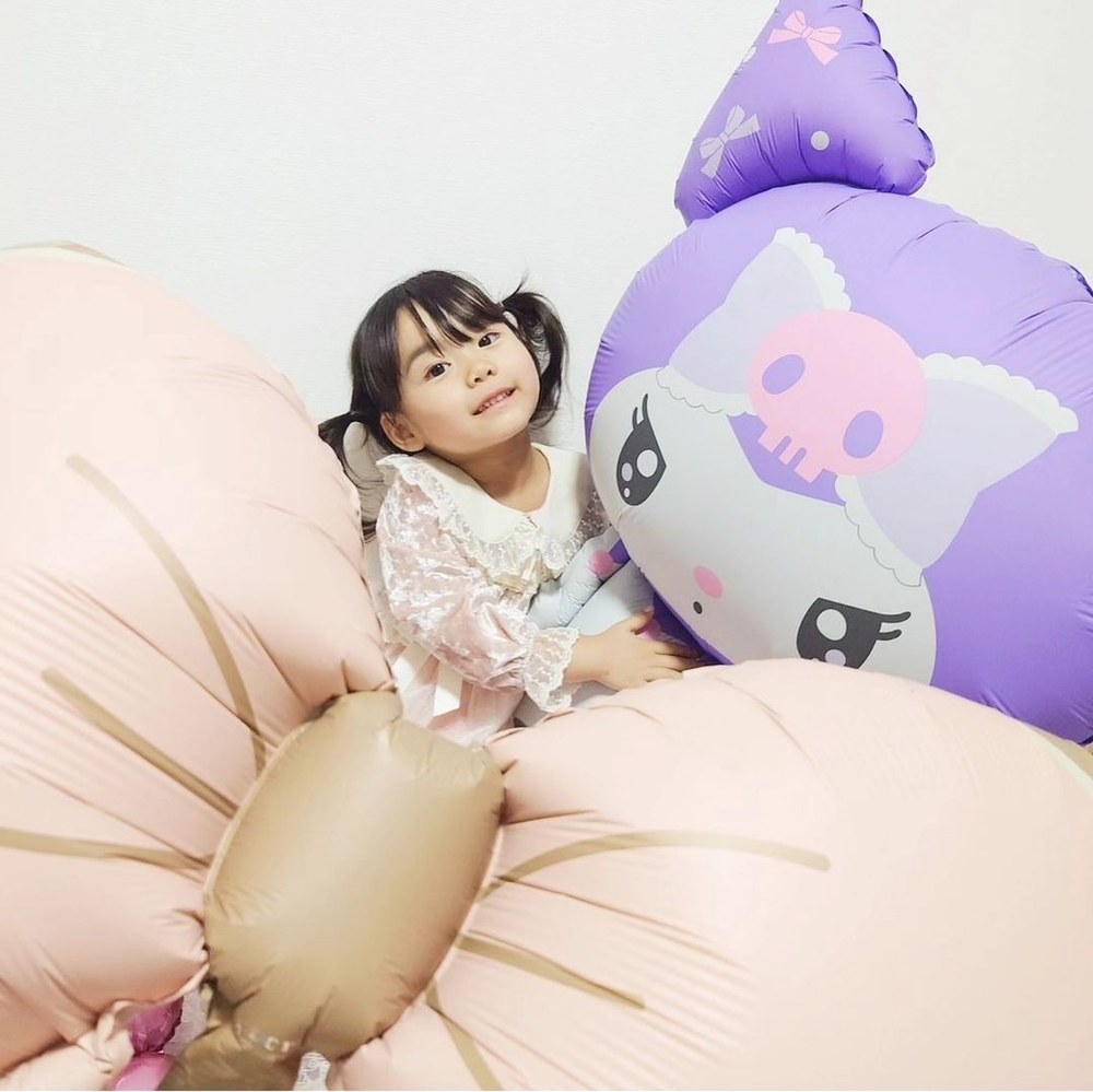 ピンクのリボンバルーンの横で、特大クロミバルーンの顔に寄りそってこちらを見る子ども