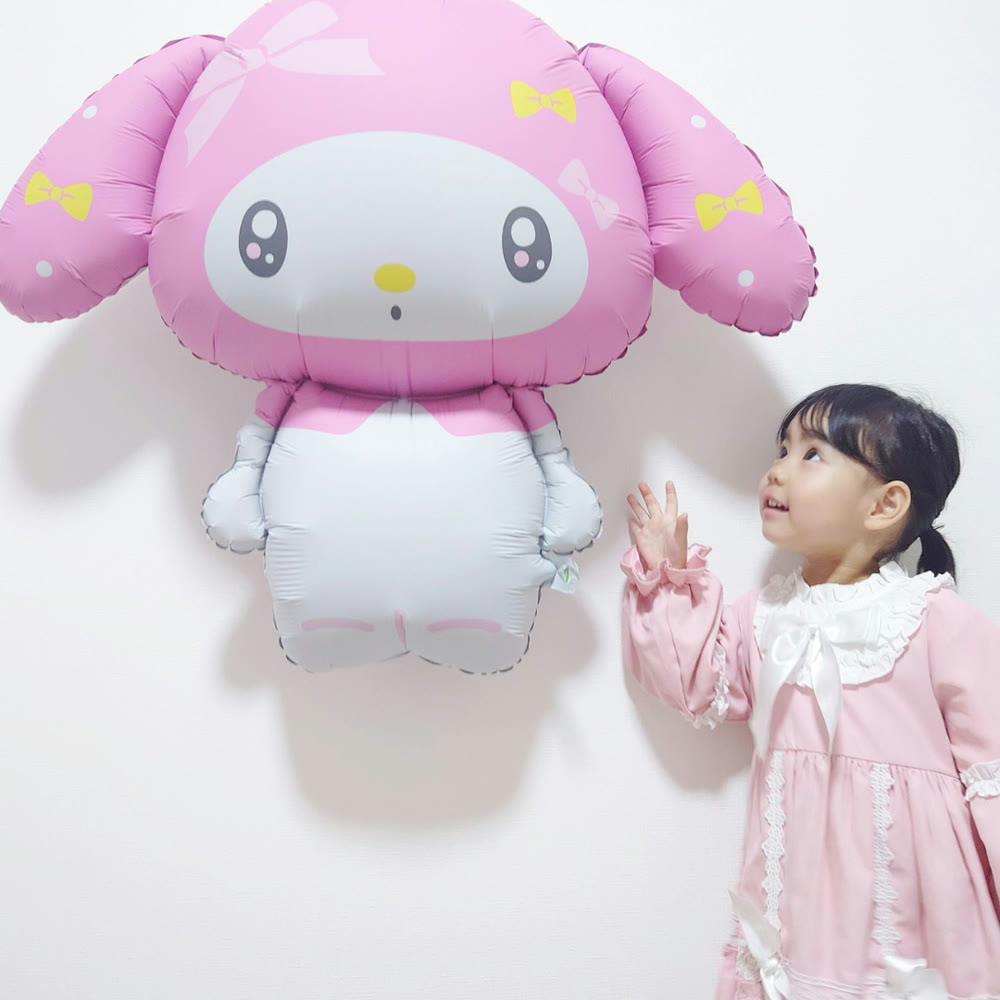 壁に飾った特大マイメロディバルーンを、ピンクのワンピースの女の子が見上げている。ほぼ同じ大きさ