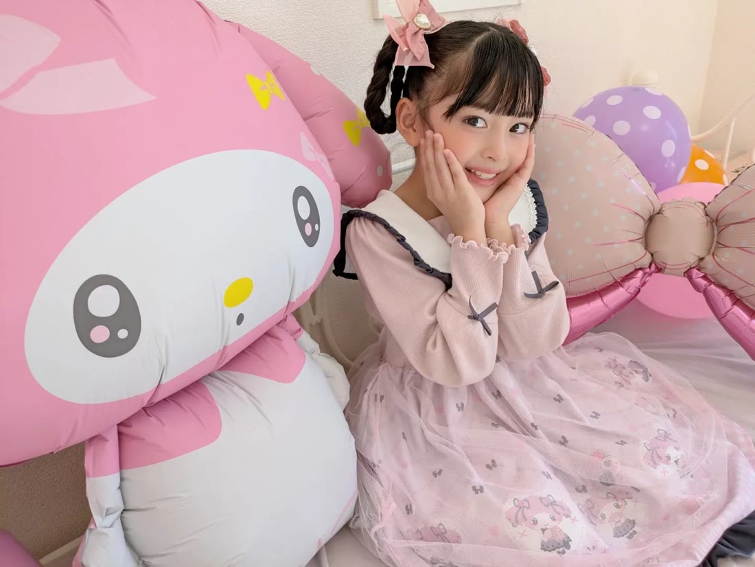 特大マイメロディバルーンとリボンバルーンに囲まれて、ほおに手を当てて笑う女の子。つや消し加工で反射がない