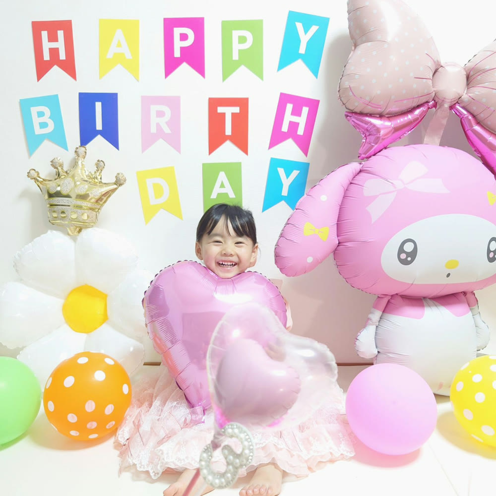 ピンクのハートバルーンを抱えて大笑いする女の子と特大マイメロディバルーン。フラワーバルーンとHAPPY BIRTHDAYガーランドの誕生日飾り付け