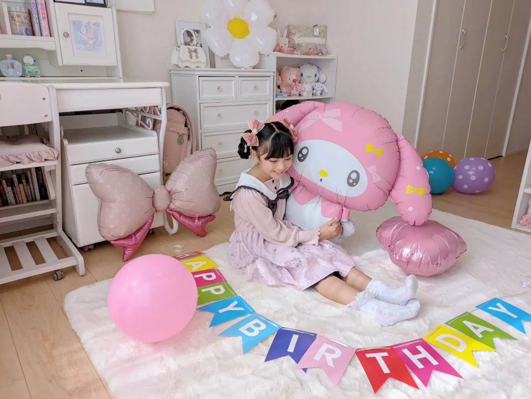 子ども部屋の床に置いた特大のマイメロディのバルーンと、それを抱きしめて笑っている子ども。床にはカラフルなHAPPY BIRTHDAYのフラッグガーランドが並べてある