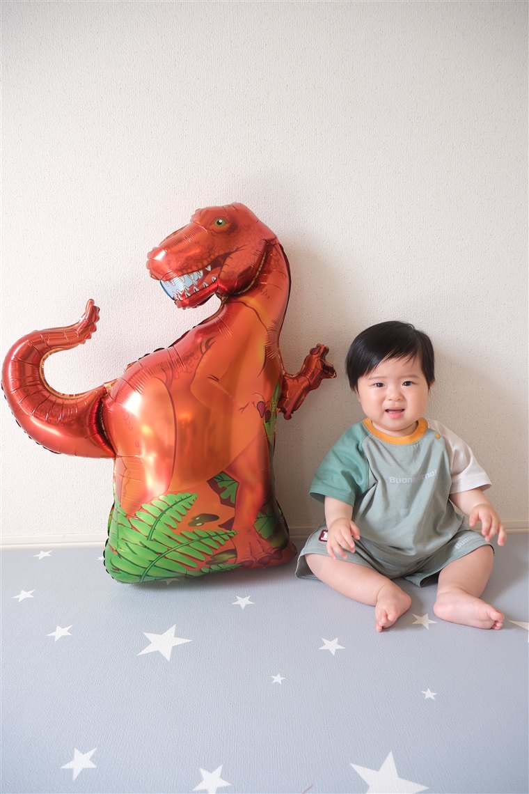 赤茶色のティラノサウルスのバルーンの横で笑う男の子