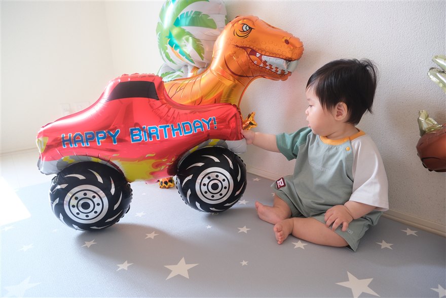 HAPPY BIRTHDAYと書かれたモンスタートラックのバルーンに手を伸ばす男の子