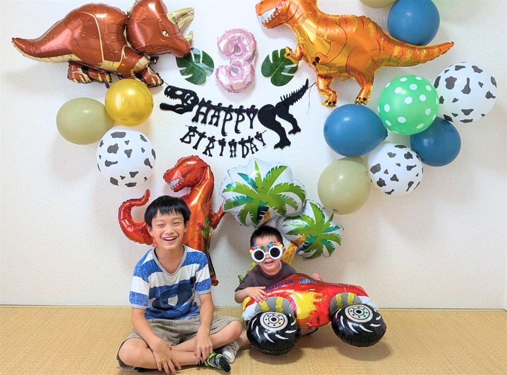 恐竜バルーンセットの前で笑顔の兄弟。3歳の誕生日をおうちでお祝い